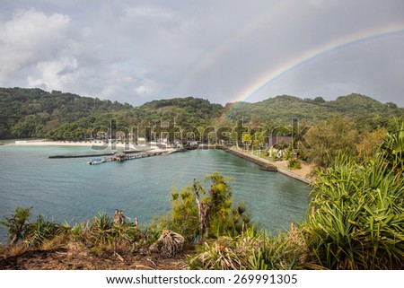 A rainbow lands on a beautiful resort on a tropical Pacific island. Rainbows are caused by sunlight refracting through raindrops.