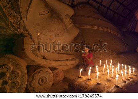 BAGAN, MYANMAR - JAN 5, 2011: Unidentified Burmese girl praying with candle light in a Buddihist temple on January 5, 2011 in Bagan, Myanmar. 89% of the Burmese population is Buddhist.