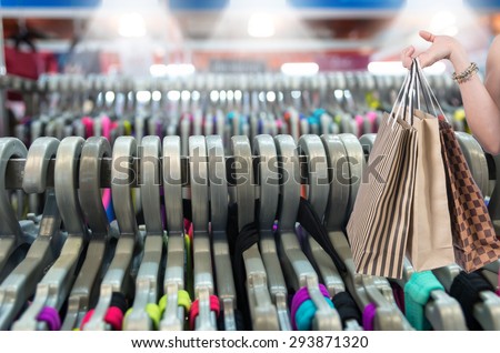 Holding shopping bags by hand on the Closeup Many Clothes hang on a shelf in a clothes store