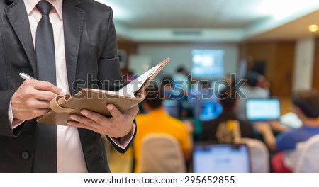 Businessman writing the note book on the Abstract blurred photo of conference hall or seminar room with attendee background