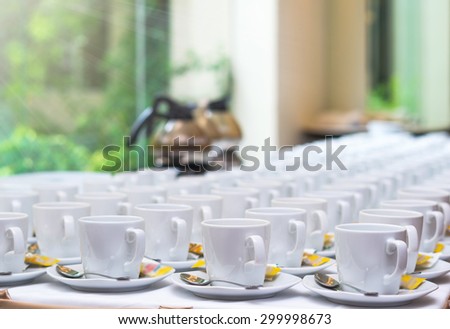 Many rows of white coffee cup with saucer and teaspoon on table and coffee maker background