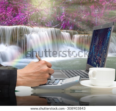 Businessman working with the laptop on Beautiful waterfall in the deep forest with rainbow,Business financial concept