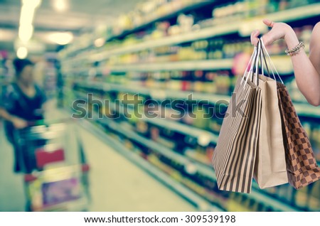 Holding shopping bags by hand on Supermarket with Abstract blurred photo of store with trolley in department store bokeh background