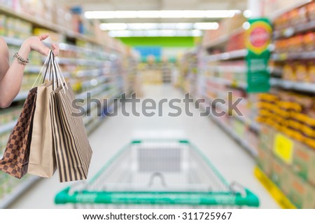 Holding shopping bags by hand on Supermarket with Abstract blurred photo of store with trolley in department store bokeh background