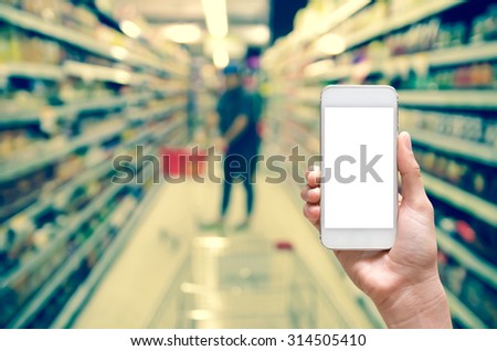 Female hand holding mobile smart phone touch screen on Abstract blurred photo of store with trolley in department store bokeh background