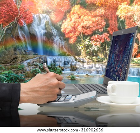 Businessman working with the laptop on Beautiful waterfall in the deep forest with rainbow,Business financial concept