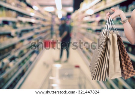 Holding shoping bags by hand on Supermarket with Abstract blurred photo of store with trolley in department store bokeh background