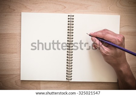 Hand holding Pencil and writing on the open leather book with wooden background