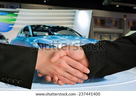 Business handshake closing a deal with car exhibition background