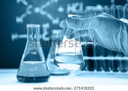 Conical flask in scientist hand with lab glassware background, blue tone