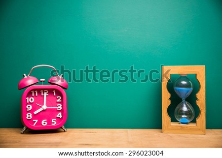 pink retro alarm clock and sand glass with green board background