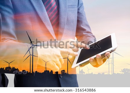 double exposure businessmen using tablet at meeting and silhouette of wind turbine at sunset