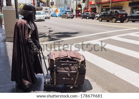 Los Angeles, CA, USA - MAY 27 2013: Person dressed as fictional character Darth Vader is crossing the street carrying luggage