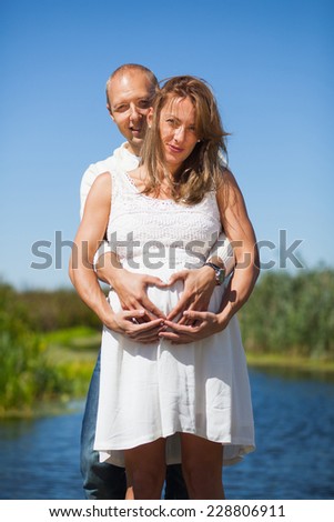 A husband and his pregnant wife holding each other and making a heart shaped form with their hands