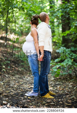A husband and his pregnant holding each other while standing back to back
