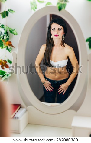 Closeup of a fit  woman in bra looking in the mirror and holding hands on jeans