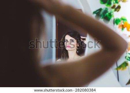 Pose from back of a sensual woman looking in the mirror and holding her hair with hand