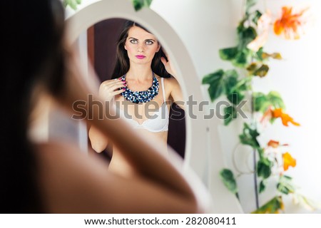 Beautiful woman in bra looking in mirror and holding her hair with hand
