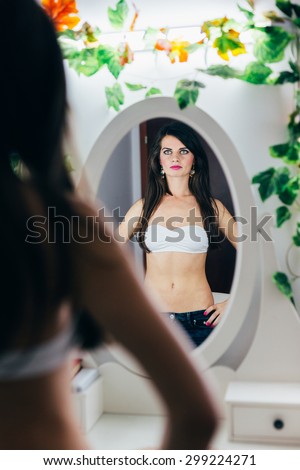 Brunette fit woman wearing a white bra looking in the mirror