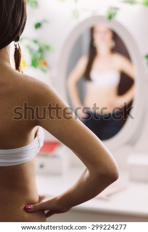 Blurry torso of a brunette woman\'s shoulder and back while looking in the mirror. Focus on the woman\'s back