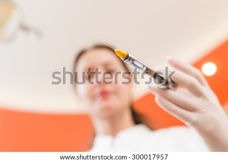 Woman dentist holding a syringe, face blurred