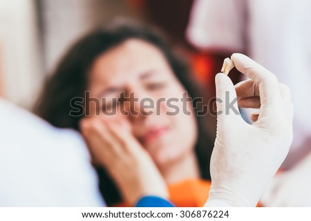 Blurry pose of a woman with toothache and a dentist hand holding the extracted tooth. Focus on the hand