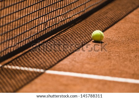 Tennis ball next to the net shot with a shallow depth of field on a clay court