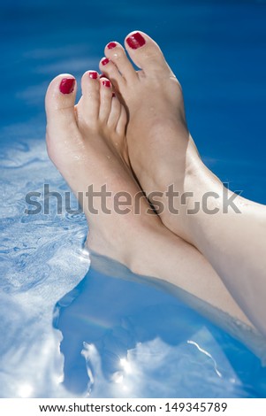 Woman Feet with nails painted red in the water at the swimming pool