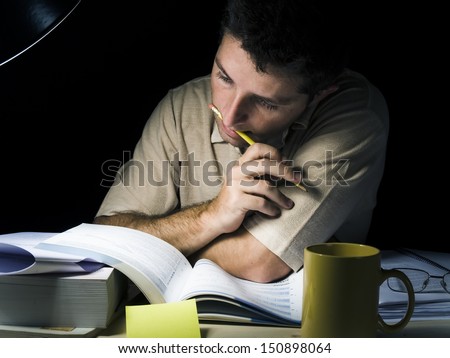 Young Man Biting Pencil Studyng at Night isolated on black background