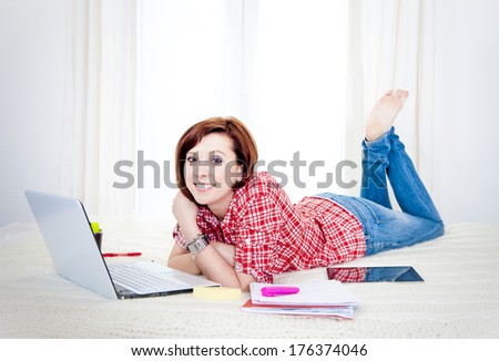 happy red haired student or business woman lying down working on her computer wearing a red shirt on white background