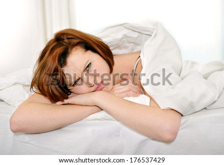 Young red hair woman lying on bed waking up with hangover and headache