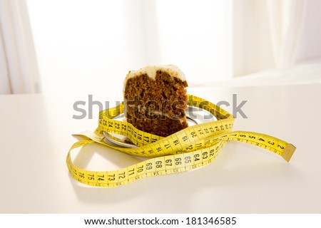 close up of carrot cake wrapped in a yellow measuring tape on a white table backlight with window in the background