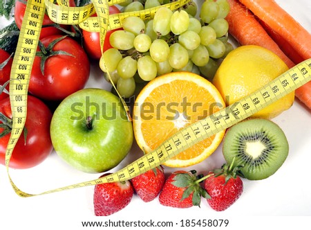 macro vegetables as tomatoes and carrots with fruit as grapes and apple wrapped in measure tape in diet , weight loss and healthy nutrition concept isolated on white background