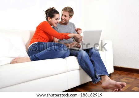 young happy couple sitting on a sofa or couch working or having fun together using internet for online shopping with computer at living room