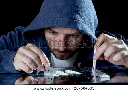 depressed sick looking Cocaine addict man, sniffing cocaine using razor blade for cutting the drug and rolled banknote to snort the white powder
