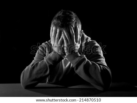 young wasted man with hands covering face suffering deep depression, pain, emotional disorder, grief and desperation concept isolated on black background with grunge studio lighting in black and white