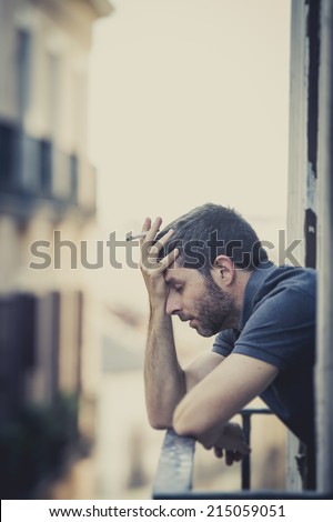 young man alone outside at house balcony terrace smoking depressed, destroyed, wasted and sad suffering emotional crisis and depression on urban background vertical format