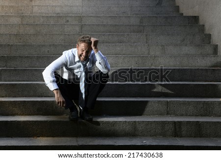 Young business man crying abandoned lost in depression sitting on ground street concrete stairs suffering emotional pain, sadness, looking sick in grunge lighting