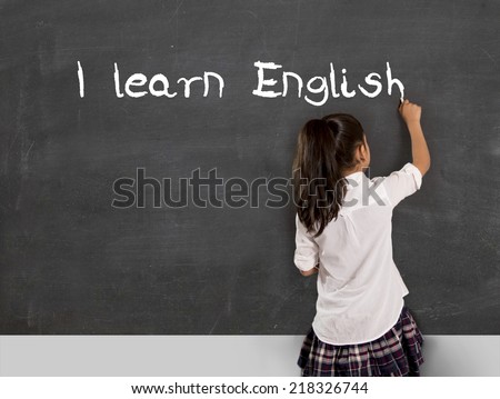 sweet little Hispanic girl at school lesson with ponytail and uniform writing with chalk on classroom blackboard in English learning , wisdom and successful education concept
