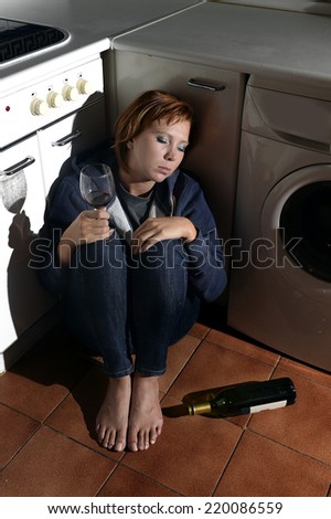 lonely drunk alcoholic sick woman sitting on kitchen floor in depression feeling miserable holding his legs in barefoot looking desperate in alcoholism and drinking to forget concept