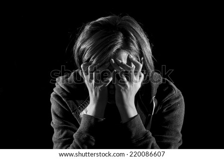 young woman suffering depression and stress alone in pain and grief covering face with hands feeling sad and desperate isolated on black background in studio lighting black and white