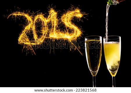 Bottle filling Champagne Glasses for celebrating new years eve 2015 with sparkling lightning numbers isolated on black background as new year greeting card