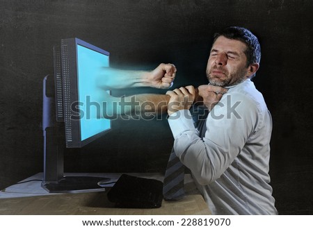 young businessman late night working at computer office arms out of screen in  neck strangling and hitting punch with fist on face in stress, overwork and business problems concept