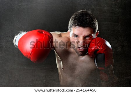 young aggressive fighter man training shadow boxing with red fighting gloves throwing vicious right hook punch in angry rage face expression isolated on black grunge dirty background