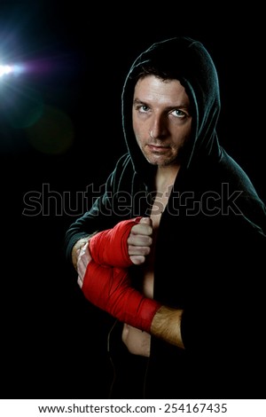 young man in boxing hoodie jumper with hood on head wearing hand and wrist wrapped ready for fighting posing isolated on black background with angry face expression