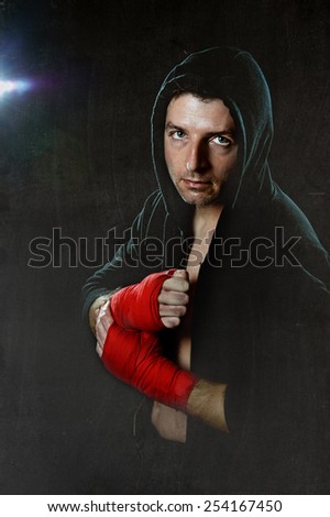 young man in boxing hoodie jumper with hood on head wearing hand and wrist wrapped ready for fighting posing isolated on black grunge dirty background with angry face expression