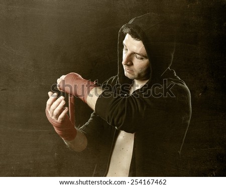 young man in boxing hoodie jumper with hood on head wrapping hands and wrists getting ready for fighting posing concentrated isolated on black  background
