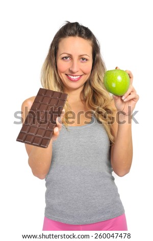 young attractive sport woman holding apple and chocolate bar in her hands in healthy fruit versus sweet junk food temptation in fitness, body health care and healthy nutrition concept