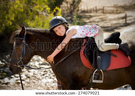 sweet beautiful young girl 7 or 8 years old riding pony horse hugging happy in  safety jockey helmet posing outdoors on countryside on summer holiday in love animal concept
