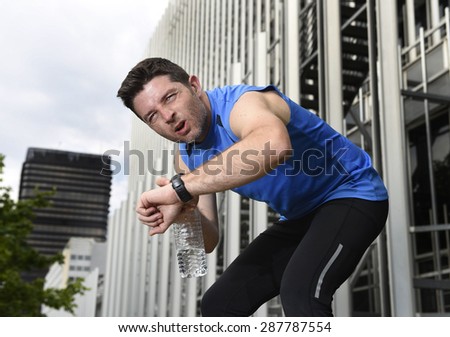 young sport man breathing exhausted after running training on city urban background leaning tired and checking timer watch in fitness and body care concept